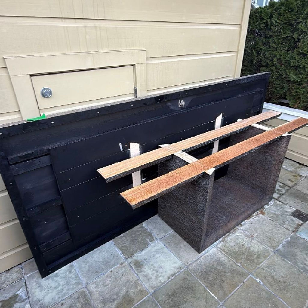 3. Disassembled rectangular dining table and parts arranged outside, next to a wall on a tiled patio.