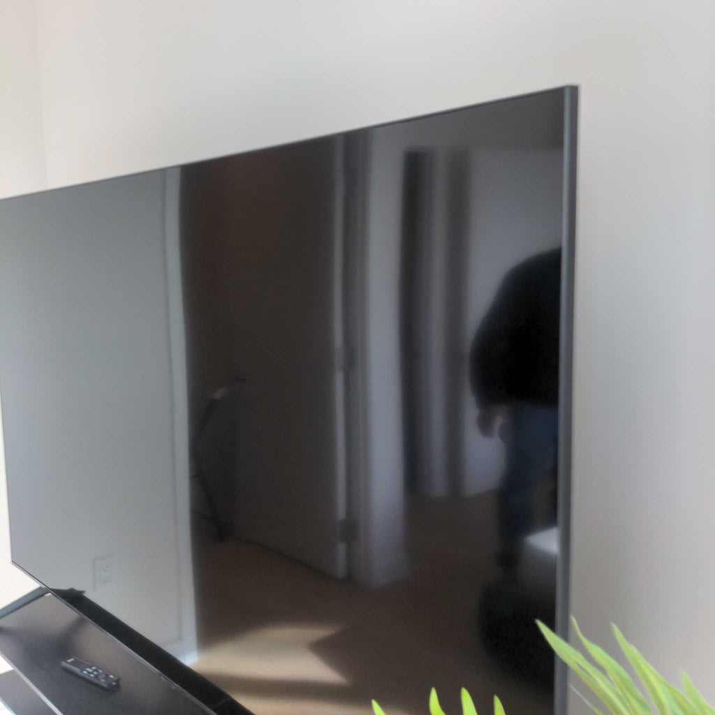 Side angle of a Reperch TV in a modern room, with its screen reflecting surroundings and remote nearby.
