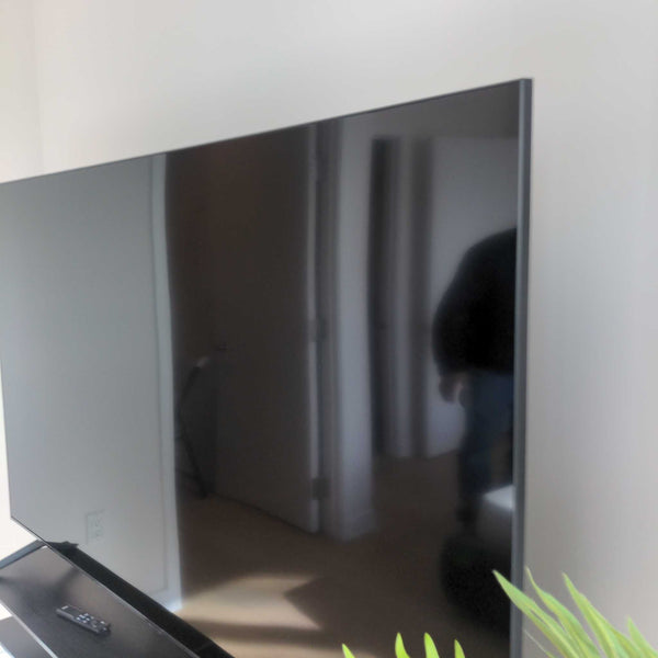 Side angle of a Reperch TV in a modern room, with its screen reflecting surroundings and remote nearby.
