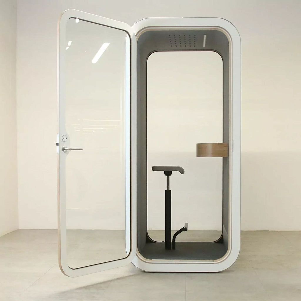 Sleek soundproof booth with a glass door, featuring a chair and table inside for privacy and focus.