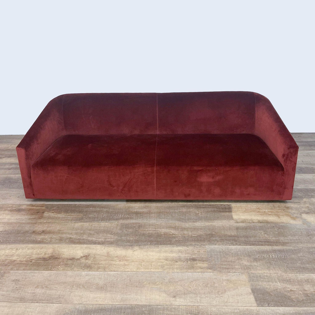 Red velvet Room and Board sofa with a curved silhouette on wooden floor.
