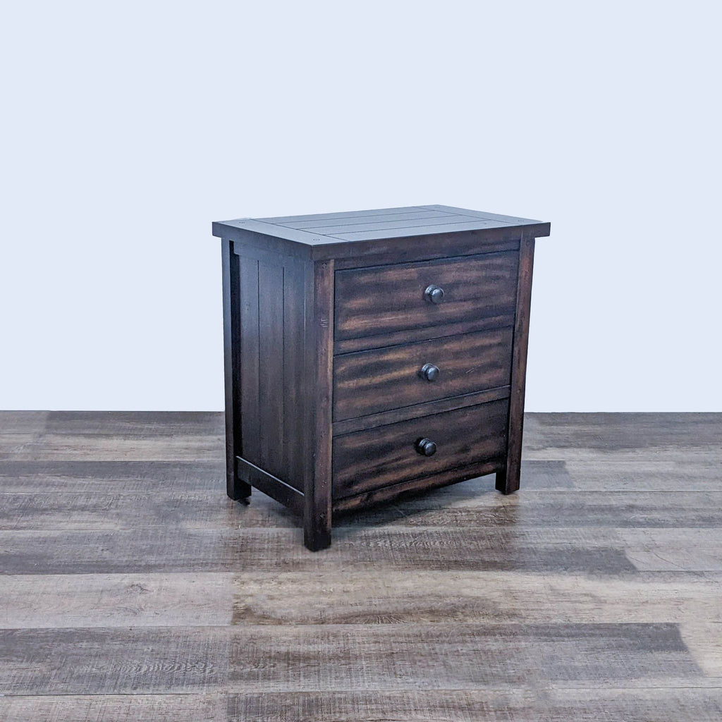 Reperch end table with planked wood top and sides, three drawers with wooden knobs on a floor.