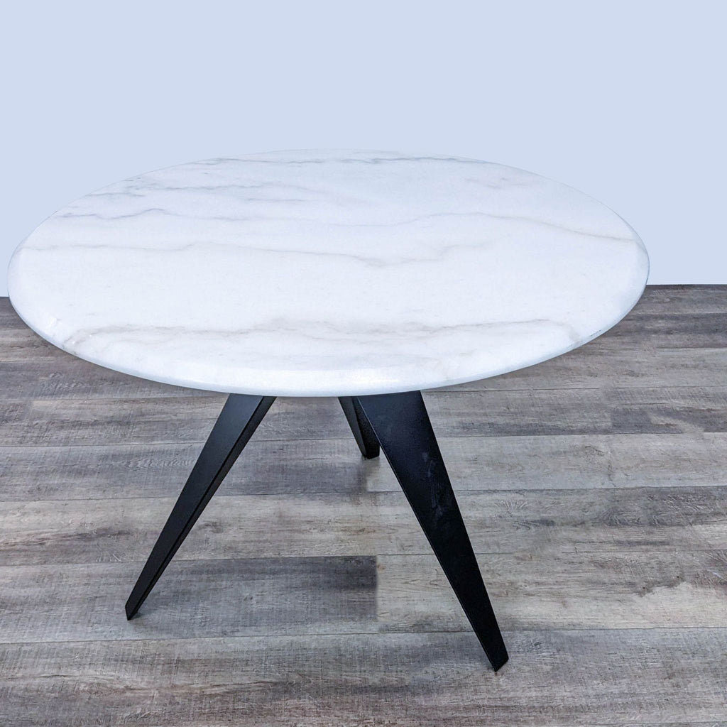 Sleek dining table from Reperch with round marble top and angular steel legs for a contemporary look.