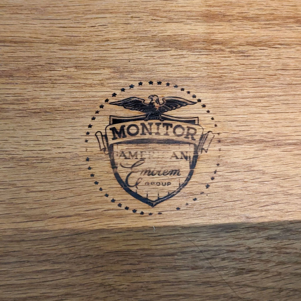 Monitor Furniture brand emblem on wood, featuring an eagle and ornate design.