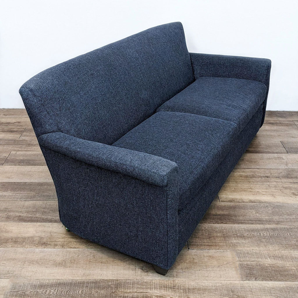 Angled view of a Crate & Barrel loveseat in dark blue, showcasing its modern design and dark feet.
