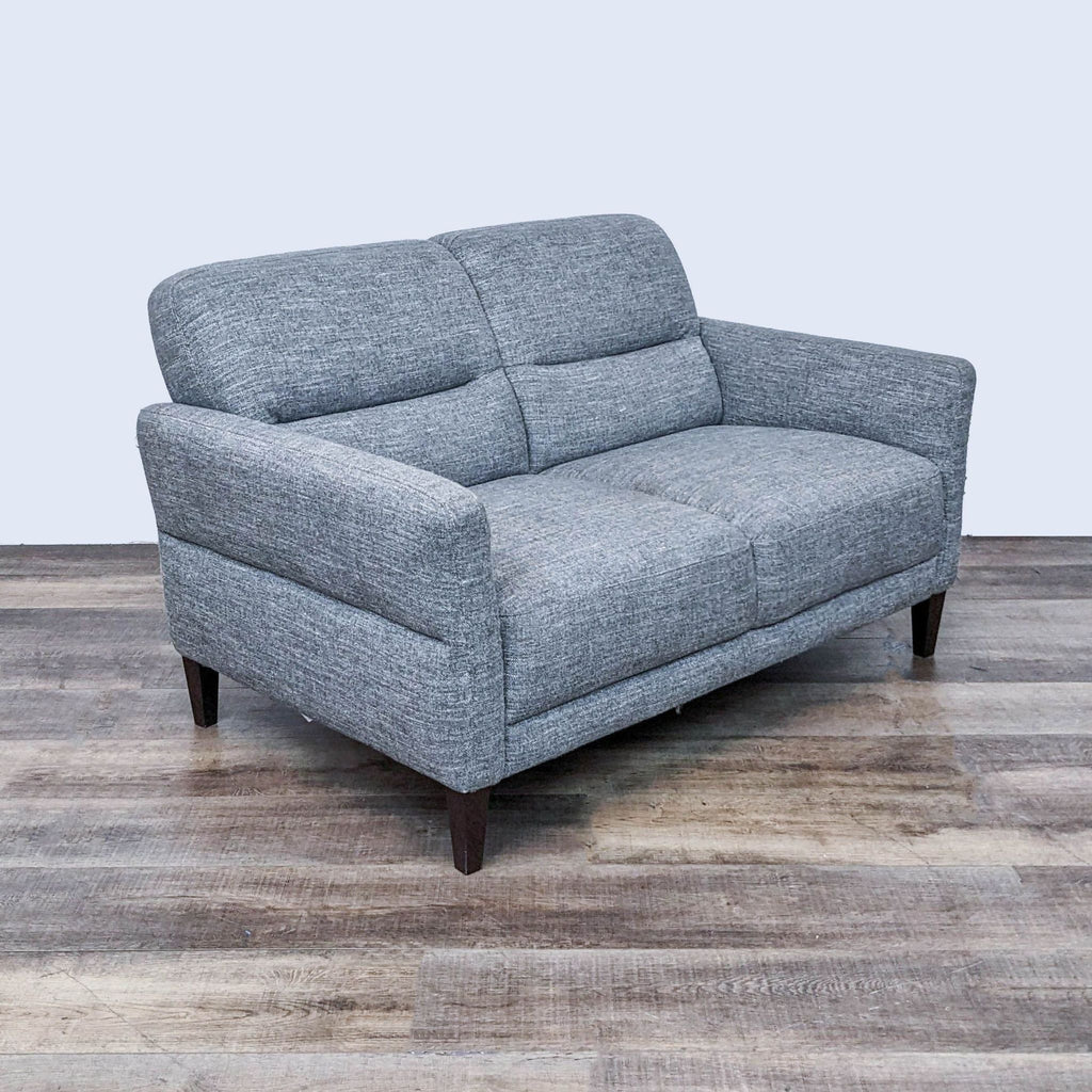 Frontal view of a gray tweed Natuzzi loveseat with line tufting and dark wood legs, set against a neutral background.