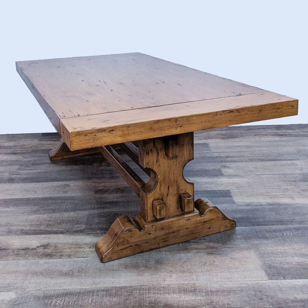 Walter and Wabash trestle base dining table with a rustic wood finish on a wooden floor.