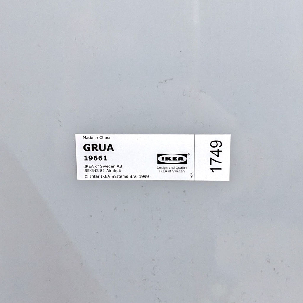 Image 2 alt: Close-up of the label on the back of an IKEA Grua mirror showing product details, mounted on a gray surface.