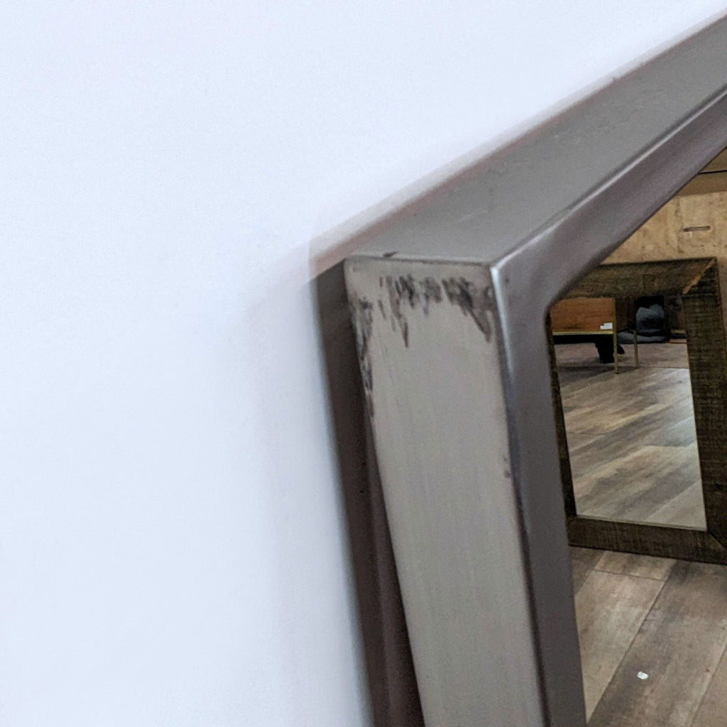 3. Detailed view of the top corner of a brushed nickel framed West Elm mirror, showing some wear.