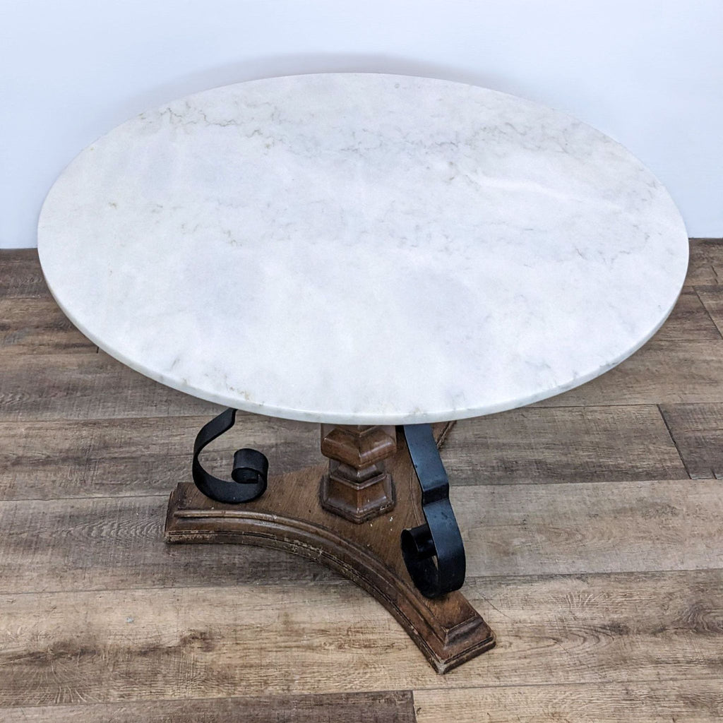Reperch dining table featuring a circular marble surface, wooden central pillar and curved metal feet.