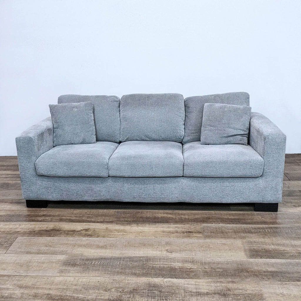 Compact gray sofa with square arms and plush cushions. Features dark wood block feet. Reperch brand.