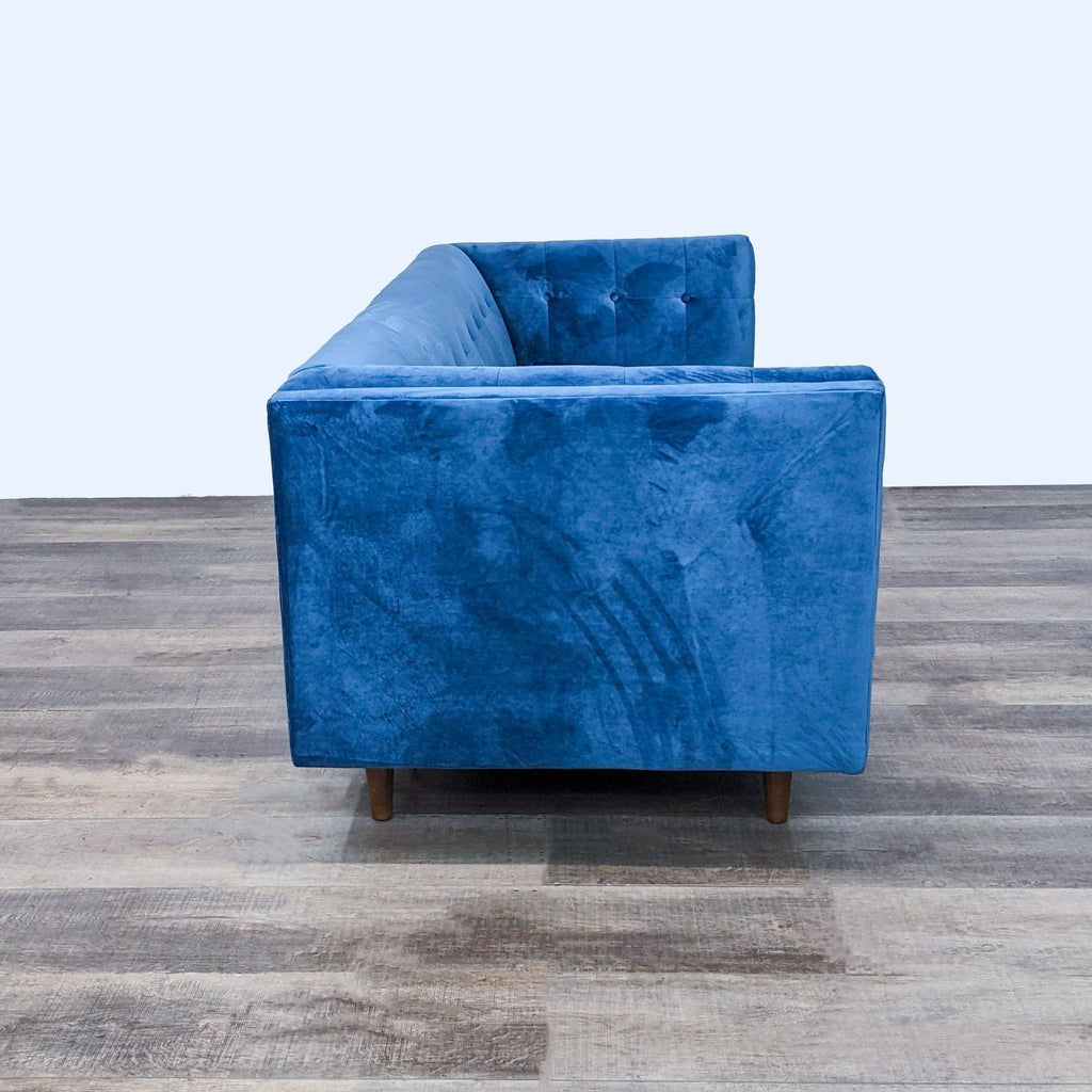 Side view of a blue velvet sofa on wood floor, showing narrow arm design.