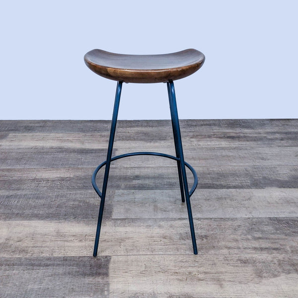 1. Counter stool with solid wood bucket seat and black steel base, designed by West Elm, shown on wood flooring.