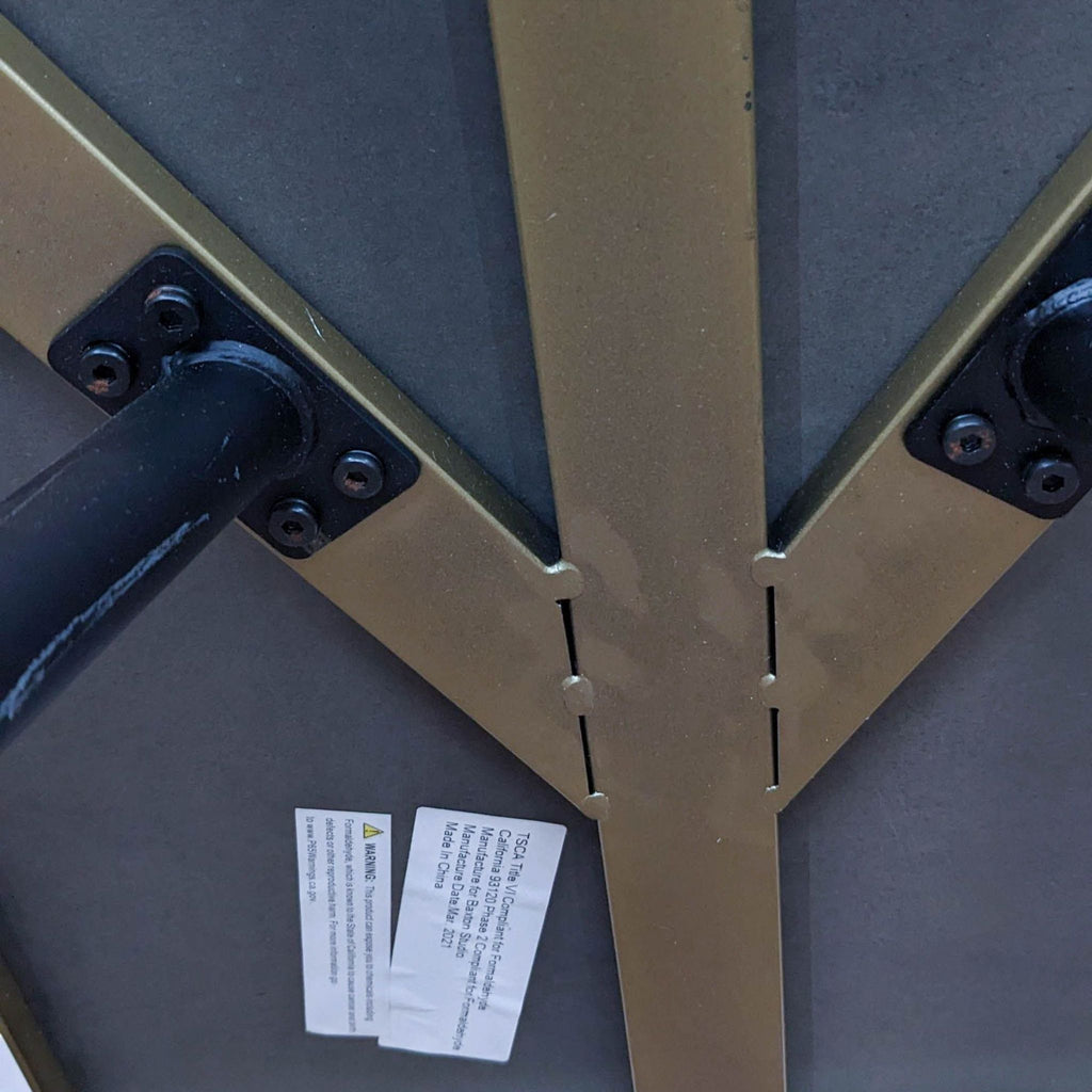 Underside view of a Baxton Studio table with metal supports and compliance labels visible.