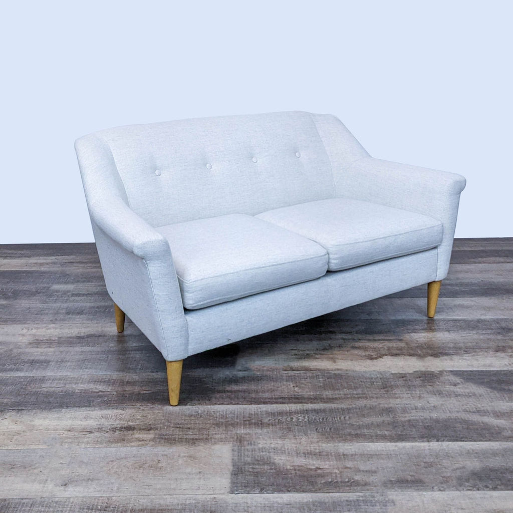 Cream fabric parlor sofa with button details and wooden legs.