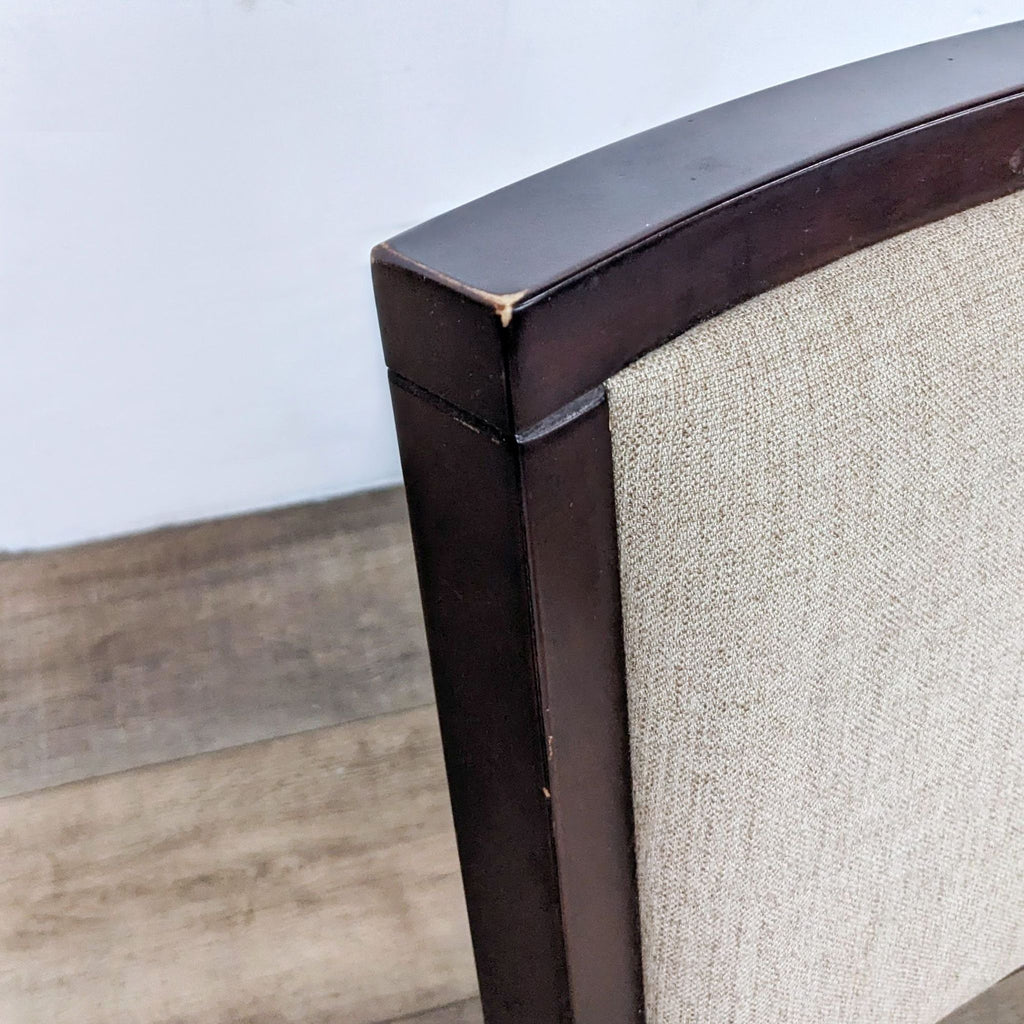 Close-up of a high-backed chair with cushioned, neutral fabric upholstery and dark wood frame.