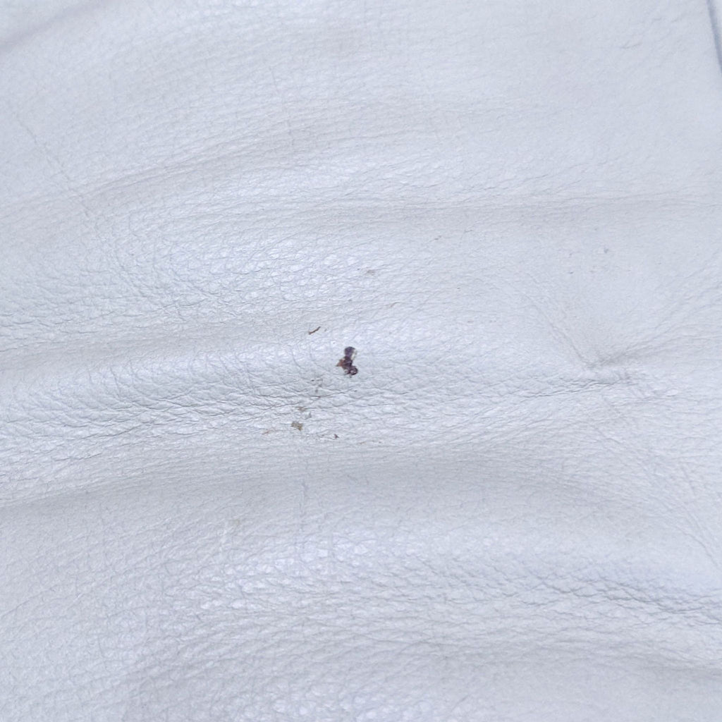 Close-up of a tan leather loveseat showing a textured surface with a small imperfection.