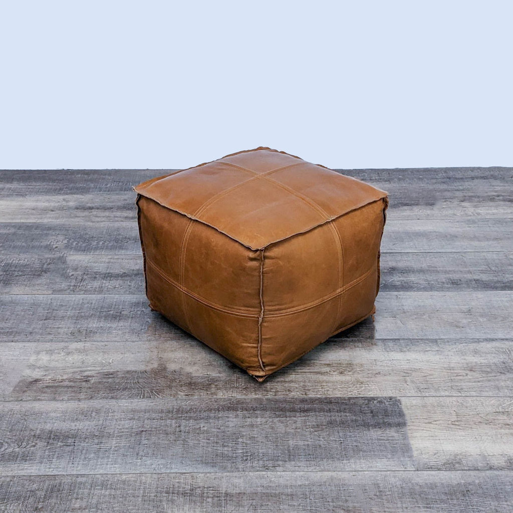 Square leather ottoman with visible stitching, seated on flooring.