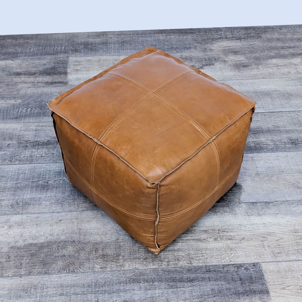 Saddle-colored 18" leather cube with self-piping on wooden floor.