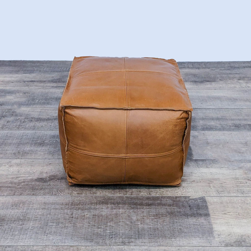 Leather cube stool in warm saddle color on a wooden surface.