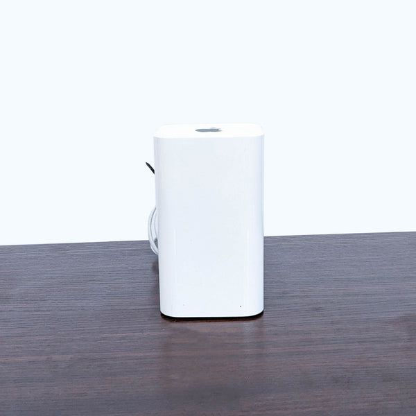 Gently used, cylindrical Apple networking device on a wooden table, minimalist design, with power cable.