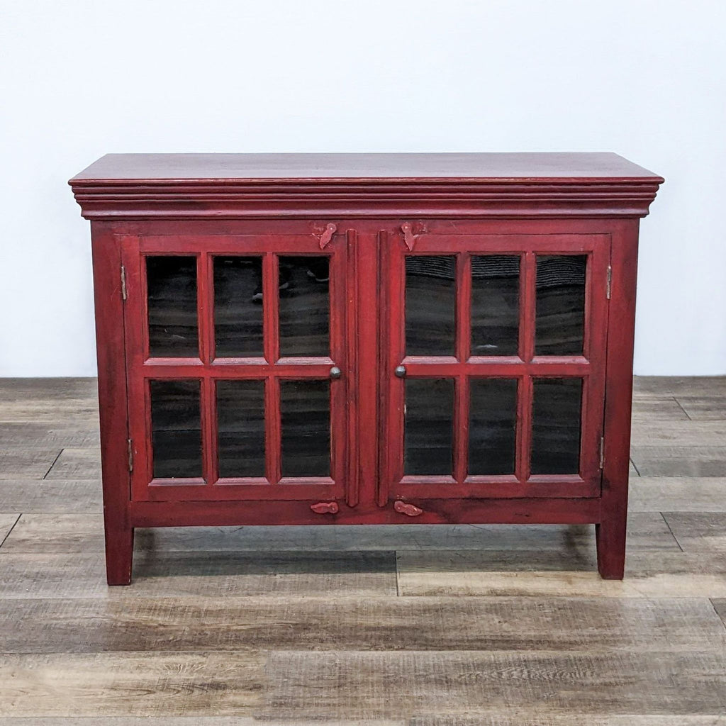Red wooden cabinet with twin glass-paneled doors on a wooden floor.