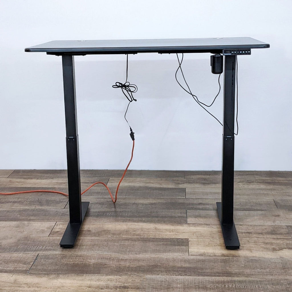 Alt text: Autonomous brand black motorized adjustable-height desk with control panel, on a steel frame against a white wall.