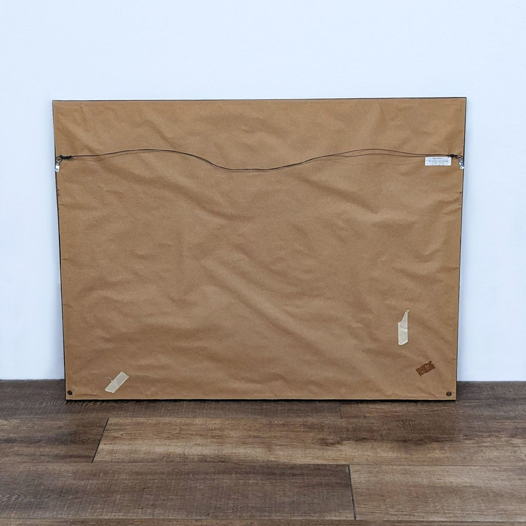 Back of a framed art piece with brown paper and hanging wire.