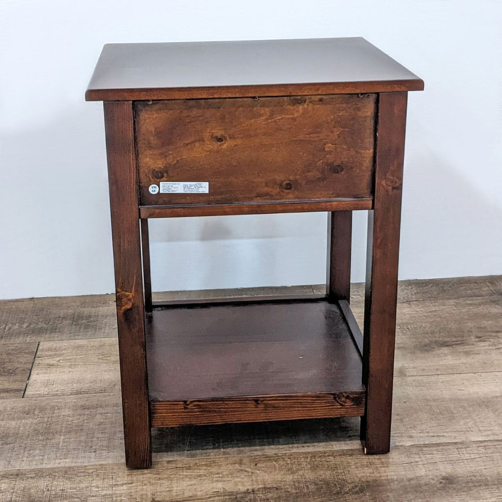 Back view of an end table with dark finish, showcasing drawer and shelf structure.