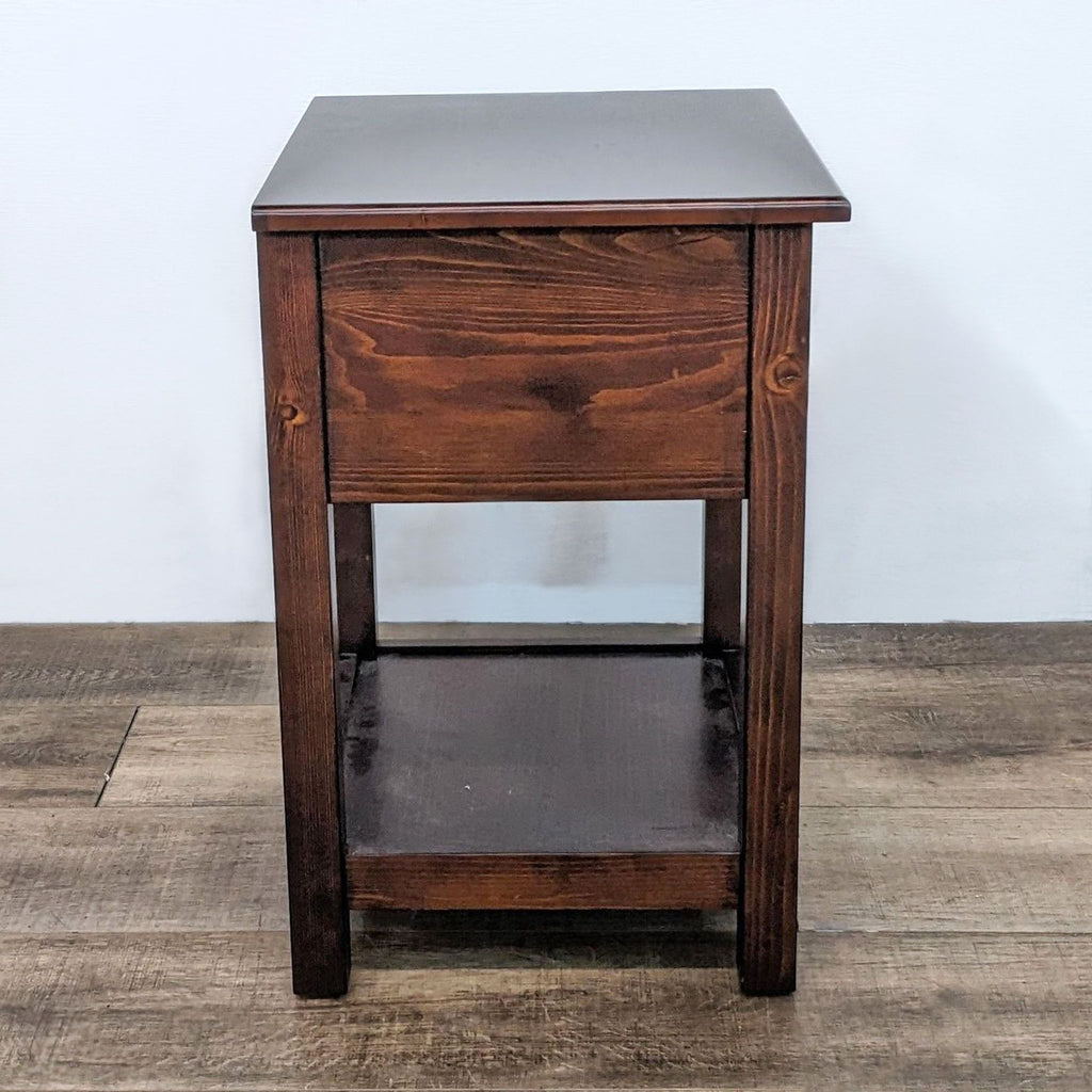 Side view of a dark wooden end table featuring a drawer and lower shelf.