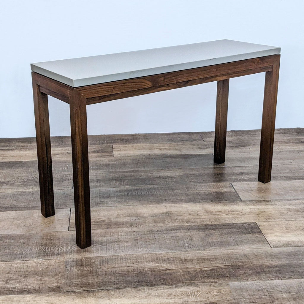 Crate & Barrel Parsons Console Table with square wooden legs and a warm grey concrete top on a wood floor.