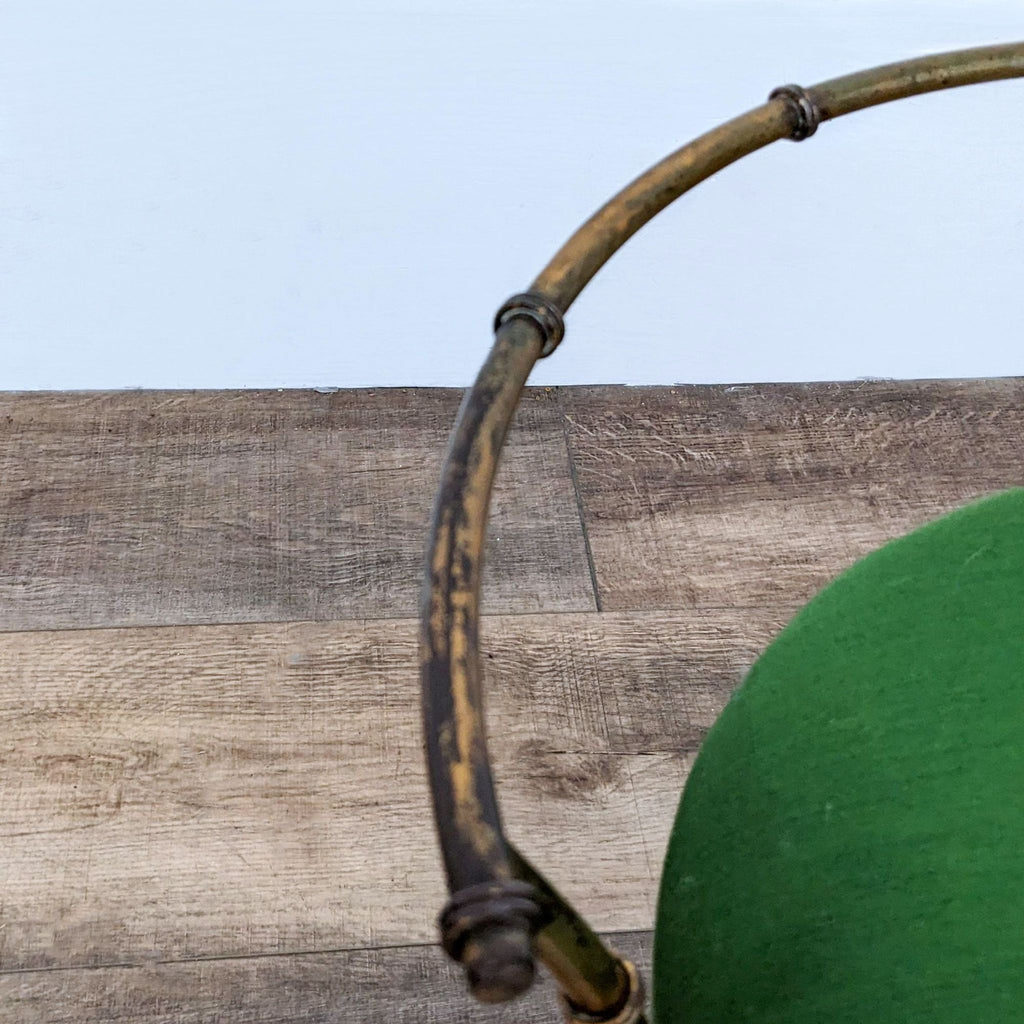 Close-up of vintage stool's gold metal frame against a wood floor background.
