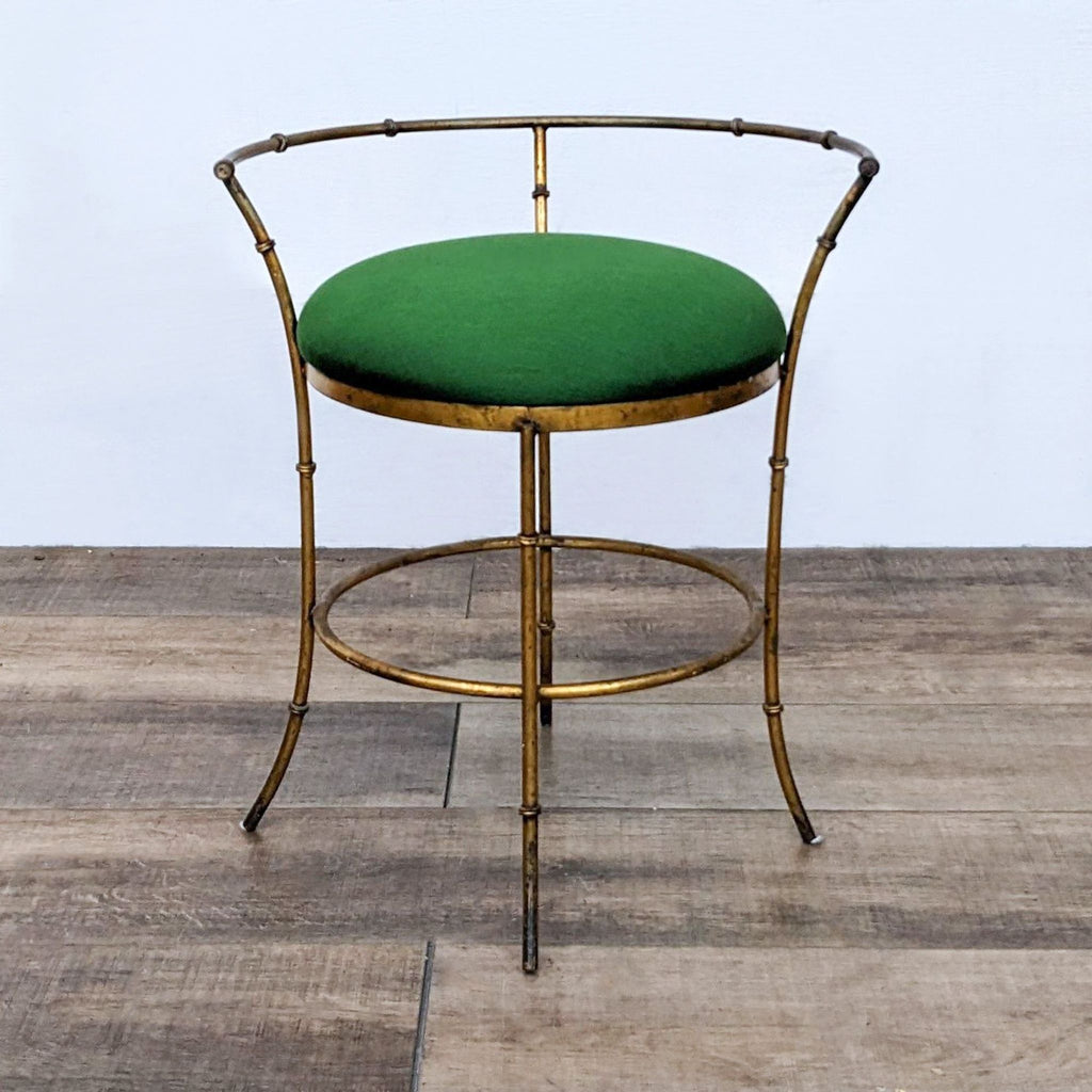 Vintage stool with a gold metal frame and a green cushion, set on a wooden floor.