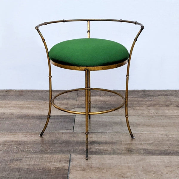 Vintage stool with a gold metal frame and a green cushion, set on a wooden floor.
