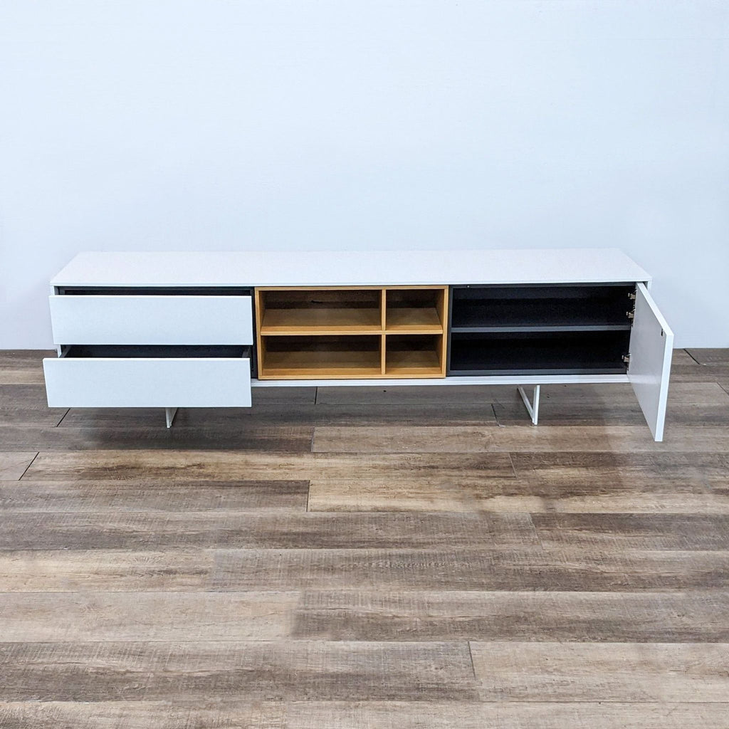 Alt text: Treku Aura Media Unit with an open-frame steel base, wood veneer, and white lacquer finish, designed by Marti and Delamo, displayed on a wooden floor.