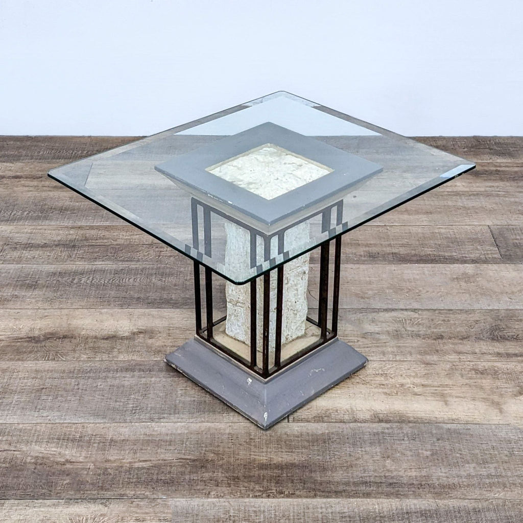 Square glass top end table with a plaster insert and metal support, set against a wood-textured backdrop.