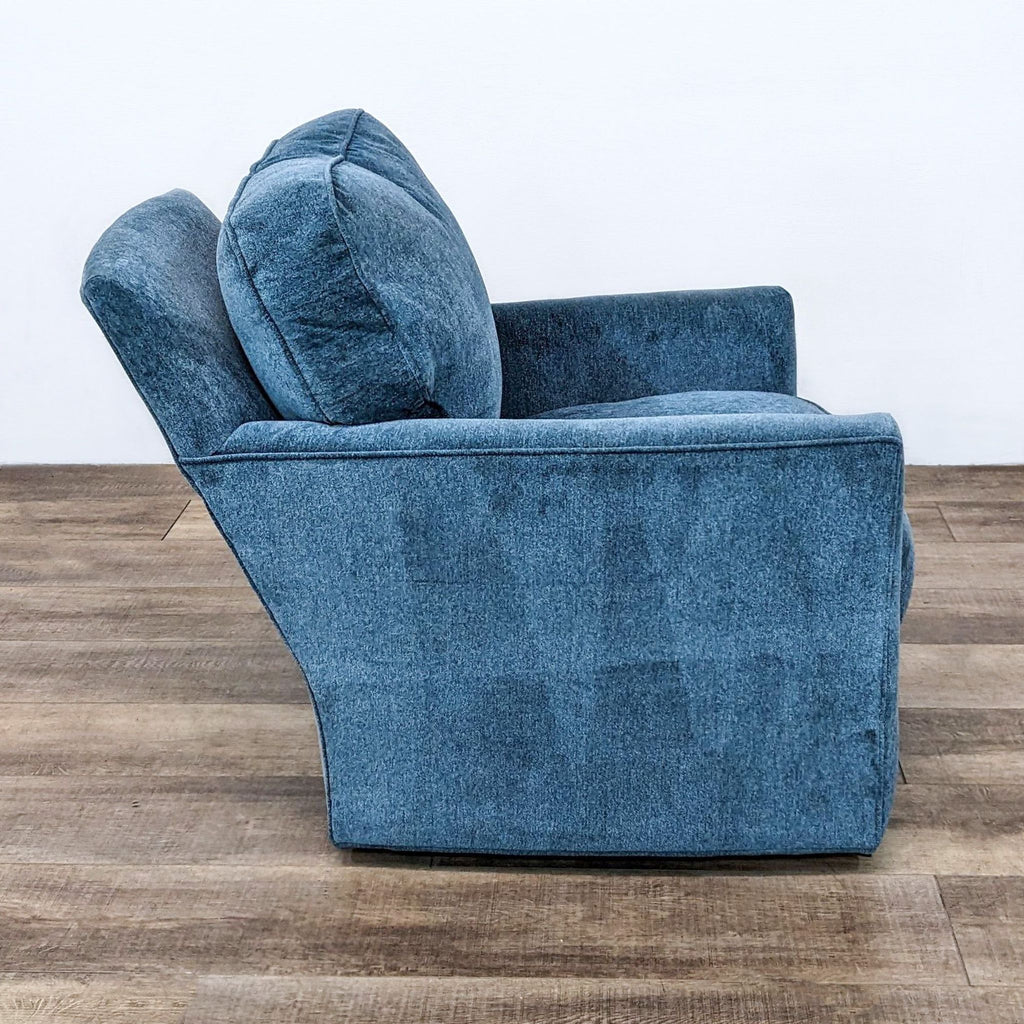 Angle view of a contemporary swivel Talia chair by Crate & Barrel, showcasing the denim-blue upholstery and wooden floor.