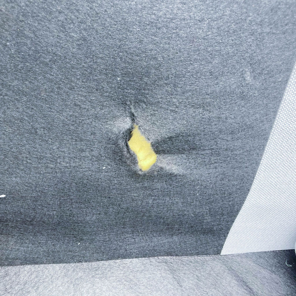 3. Image showing a tear in the gray fabric of a West Elm Eddy sofa revealing yellow foam underneath.