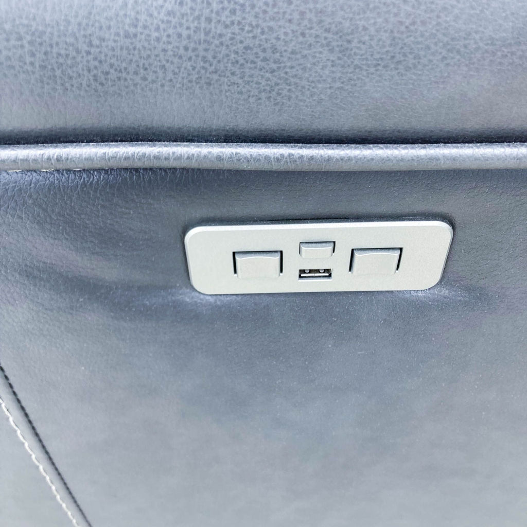 2. Close-up of a USB port built into the side of a blue Reperch power leather reclining sofa, surrounded by smooth leather material.