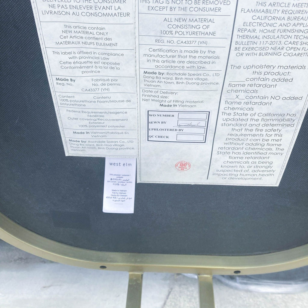 Detailed tag on a West Elm dining chair showing materials and regulatory compliance, set against fabric background.