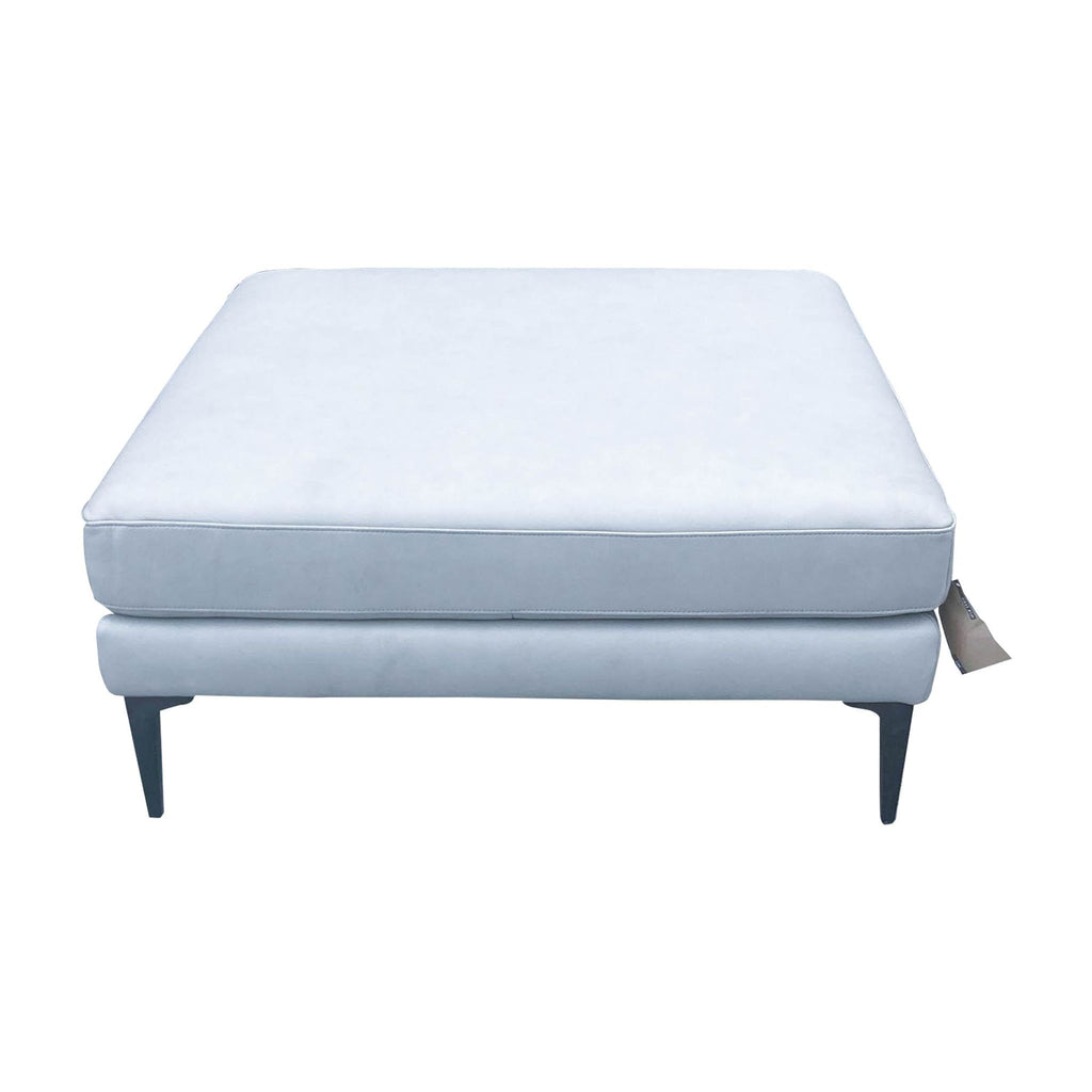 3. Profile view of West Elm's grey fabric ottoman highlighting the sleek metal legs and plush top.