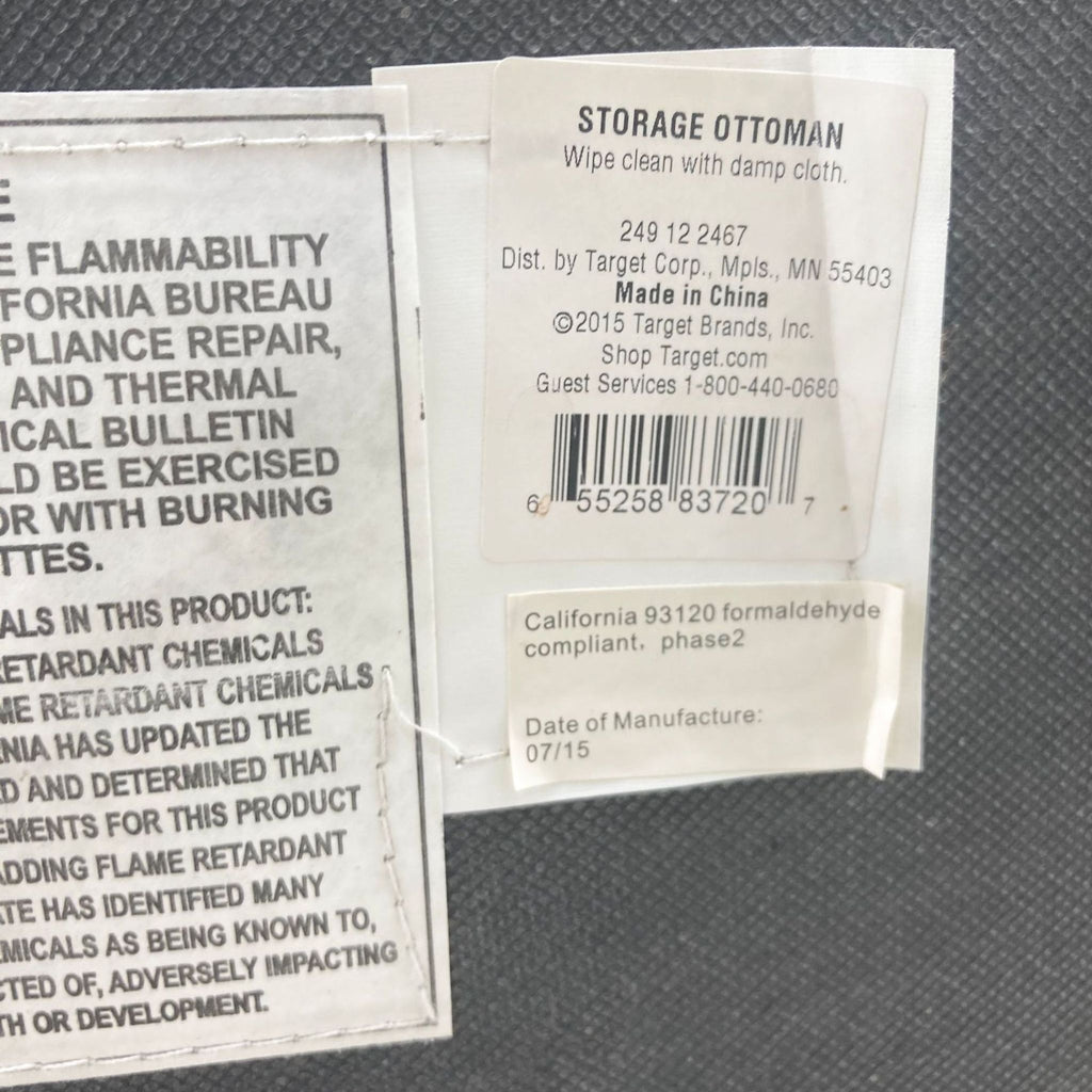 2. Close-up of the label on a Target grey fabric storage ottoman showing cleaning instructions and compliance information.