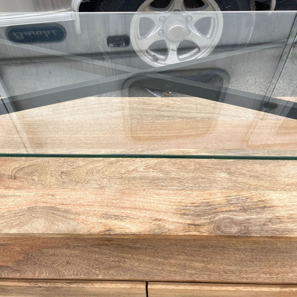 Top-down view of glass surface reflecting a reel on a West Elm console table with wooden shelves.