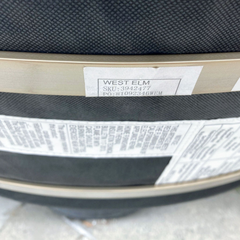 Close-up of a West Elm stool's underside label with SKU number and brand details on a black fabric surface.