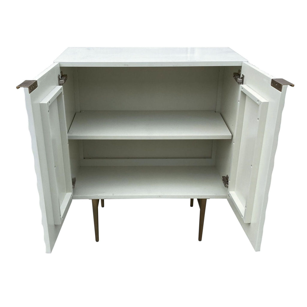 Interior view of an open West Elm parchment cabinet with shelves and brass hinges.