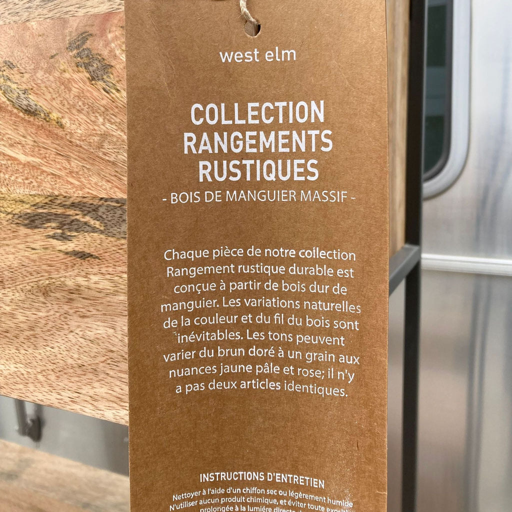 Close-up of a West Elm tag describing Rustic Storage Collection details in French, attached to the cabinet.
