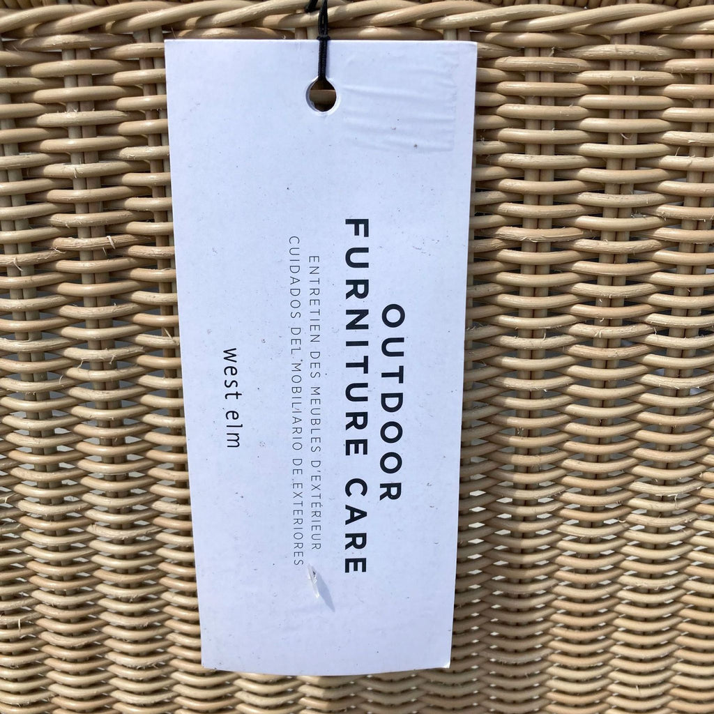 Tag with care instructions attached to a West Elm outdoor resin wicker furniture piece.