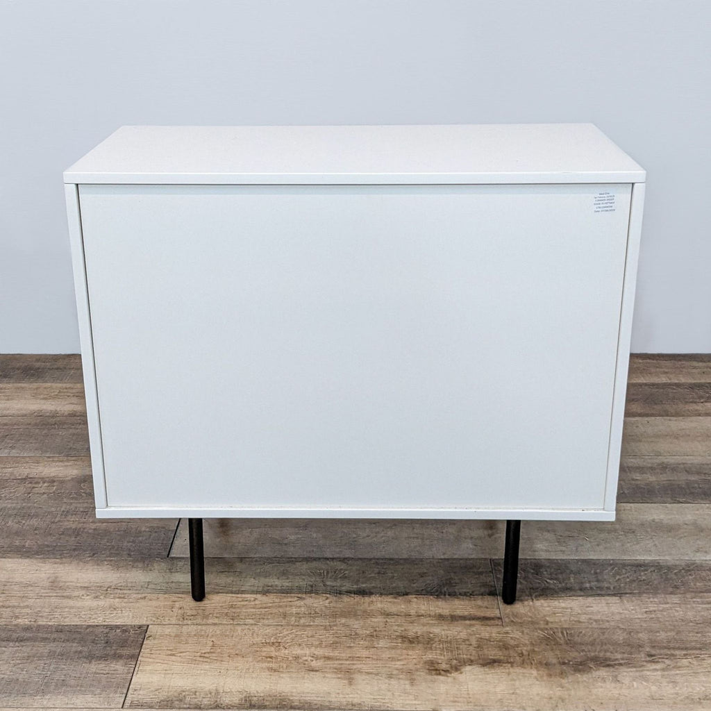 Back view of a West Elm dresser, showcasing smooth white paneling and black legs.