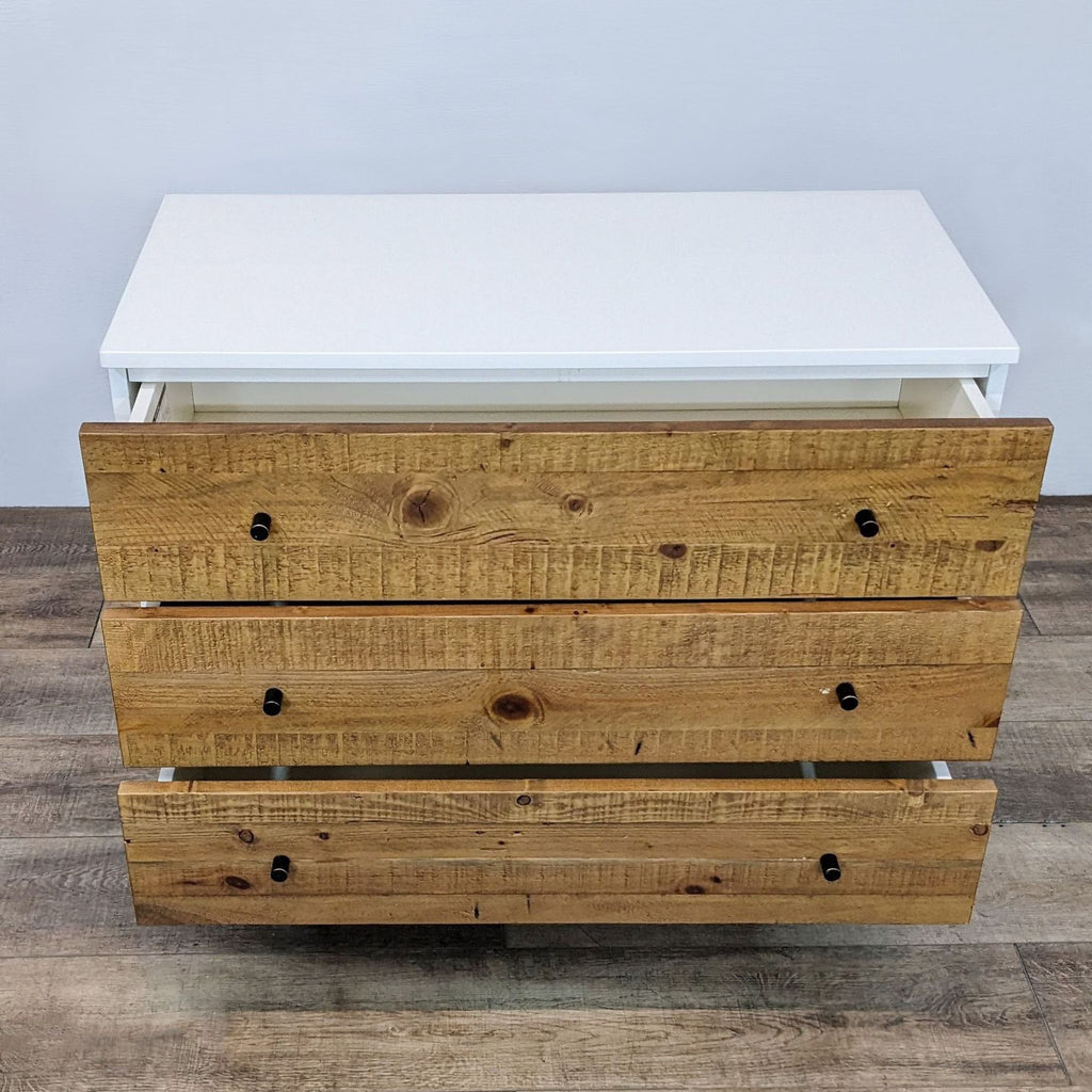 White dresser with open drawers showing a rustic wood finish and metal pulls.