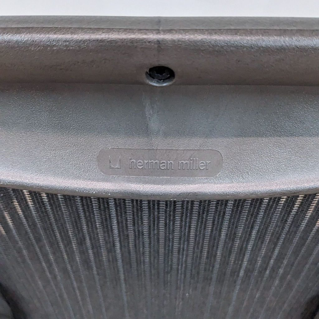 Close-up of Herman Miller logo on a black mesh backrest of an Aeron office chair highlighting brand identity.